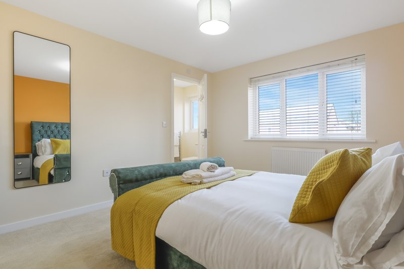 Bright bedroom with double bed, yellow accents, mirror, and shuttered window