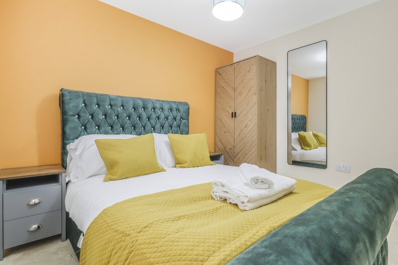 Bedroom with yellow bedding, tufted headboard, wooden wardrobe and mirror