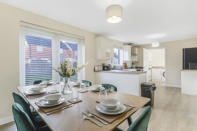 Open-plan dining and kitchen area with set table, chairs, flowers, and appliances