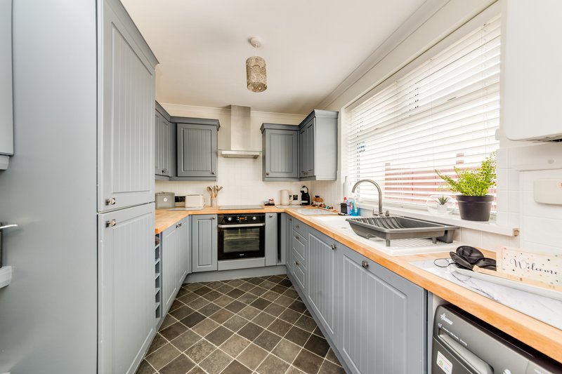 Modern kitchen with grey cabinetry, wooden worktops, built-in appliances and diagonal tile flooring