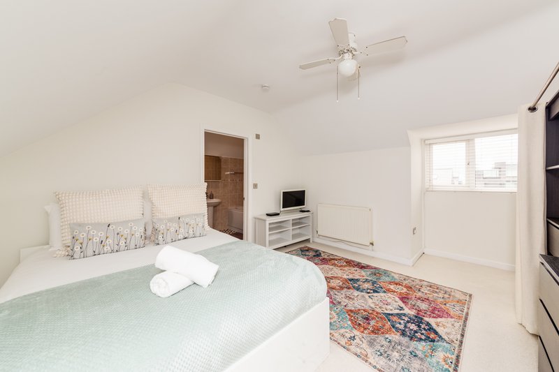 Bright bedroom with double bed, ceiling fan, TV stand, and patterned rug