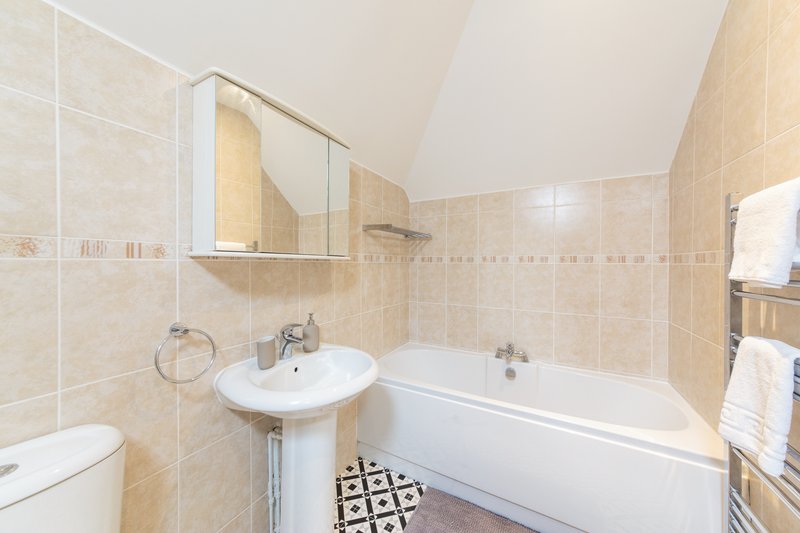 Bathroom with bathtub, pedestal sink, mirror cabinet and beige tile walls