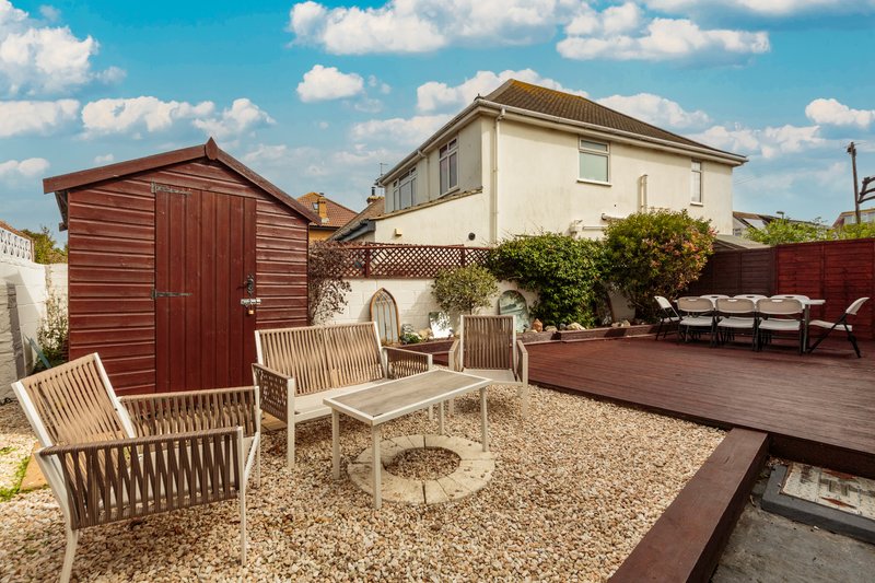 Rear garden with wooden furniture, gravel patio, decking, shed and two-storey house