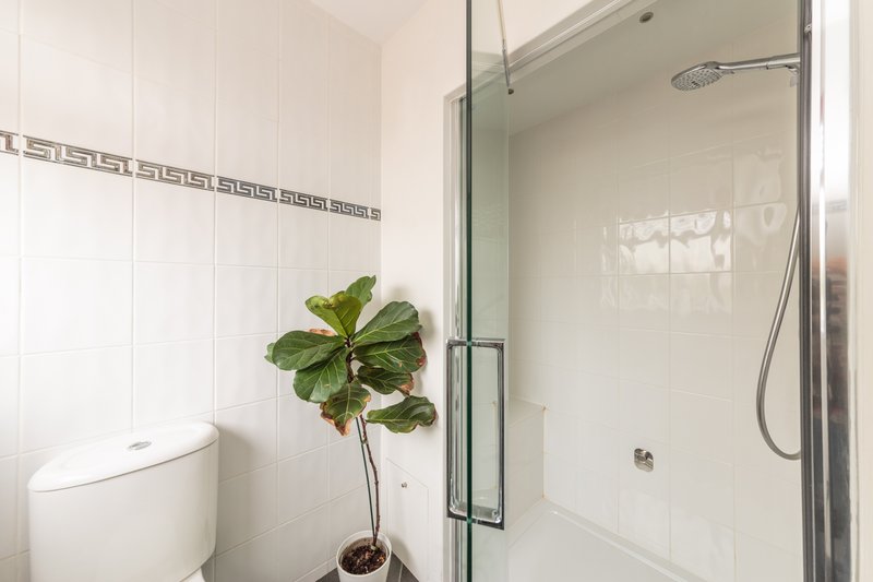 Modern bathroom with white tiles, glass shower enclosure, toilet, and potted plant