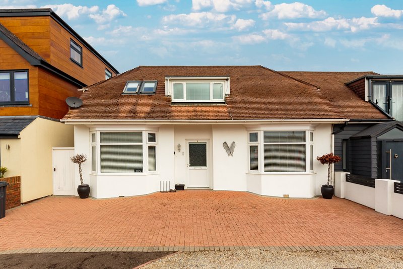 White bungalow with brown roof, driveway, front garden and neighboring properties