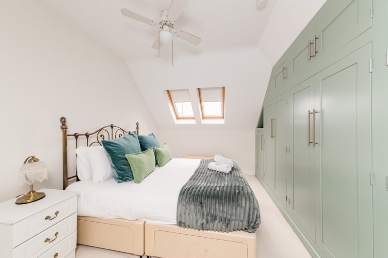 Bright bedroom with metal bed frame, green storage cabinets, skylight windows and white bedding