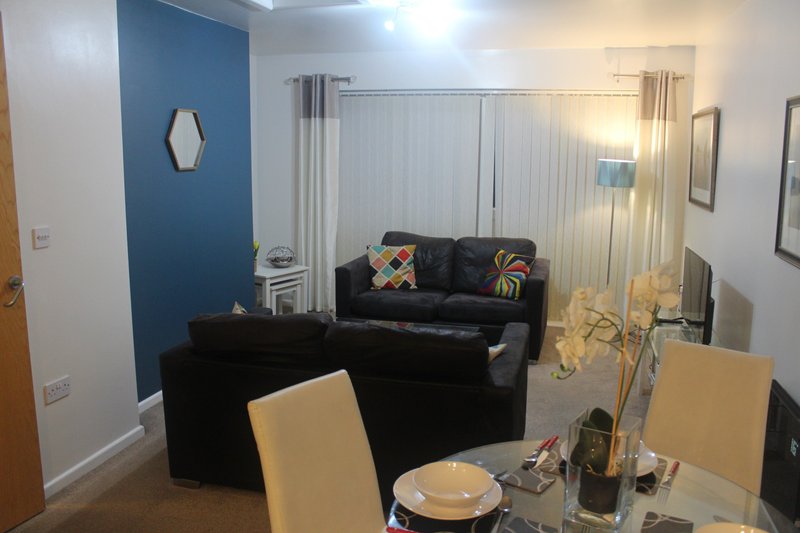 Open-plan living and dining area with black sofa, blue accent wall, and cream dining chairs