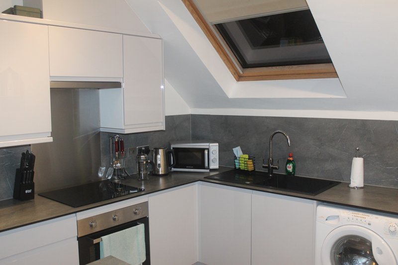 Modern kitchen with white cabinetry, black countertop, microwave, and washing machine under skylight