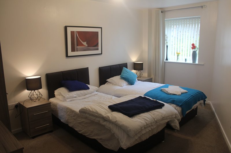 Bedroom with double bed, dark headboard, bedside lamps, framed wall art, window with curtains