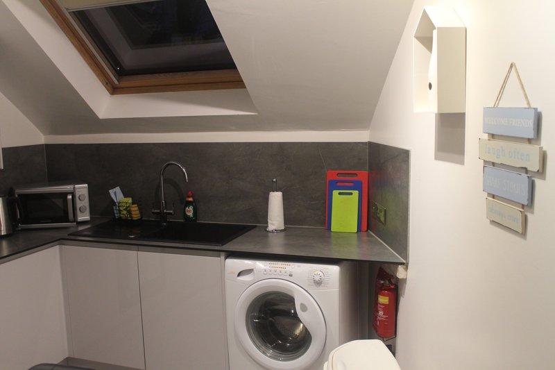 Compact kitchenette with washing machine, dark countertop, white cabinetry, and skylight window