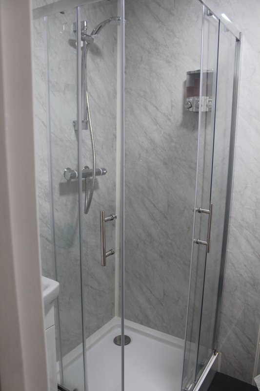 Modern bathroom with glass-enclosed shower stall, marble-look tile walls and white base