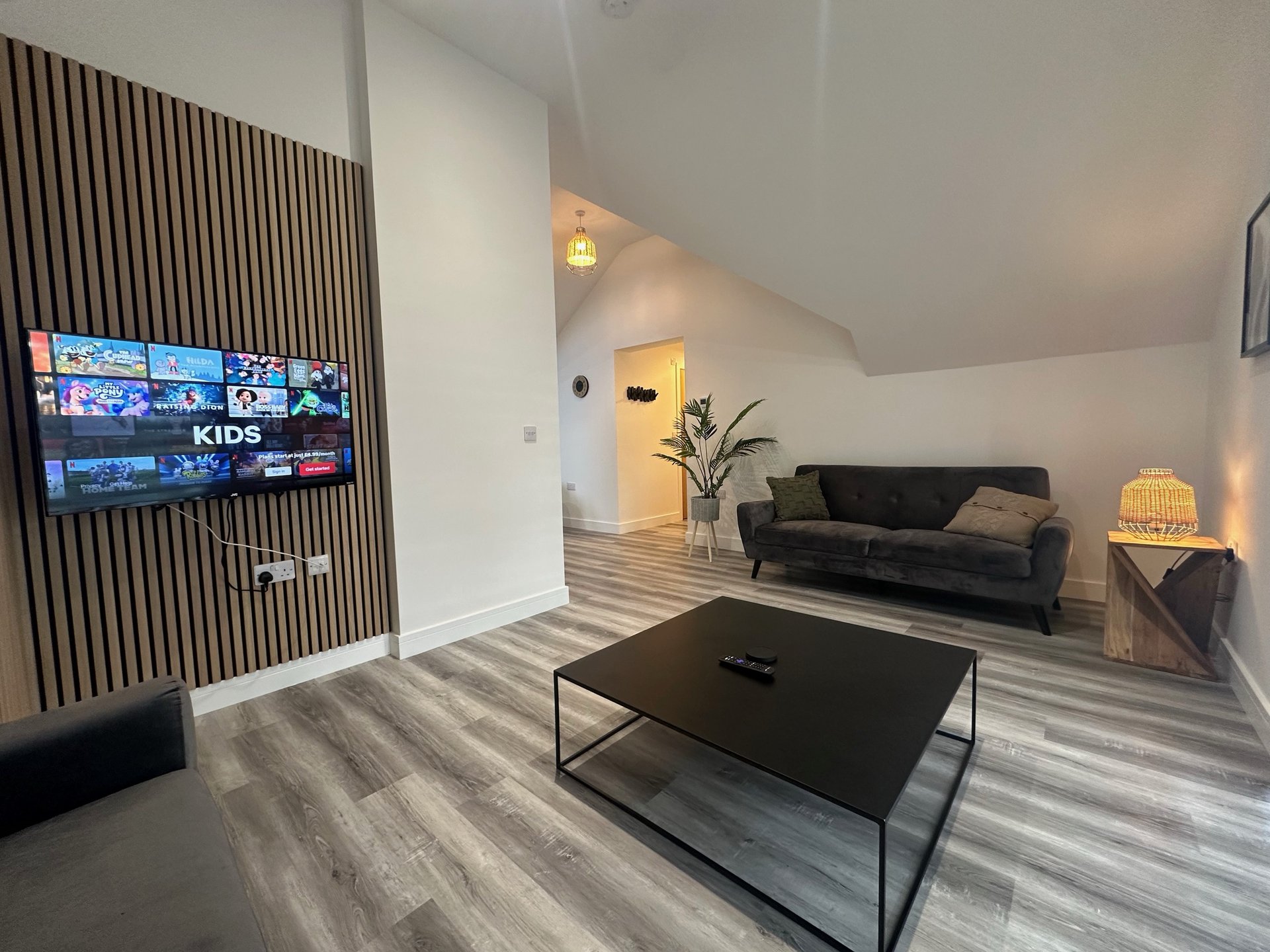 Open-plan living room with TV, black coffee table, dark sofa and wooden flooring