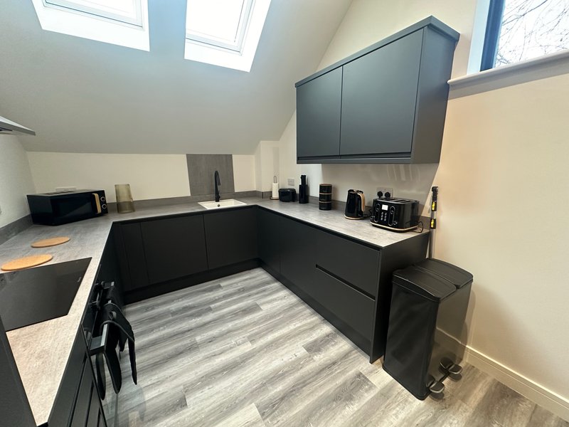 Modern kitchen with black cabinetry, white countertop, skylight, and striped flooring