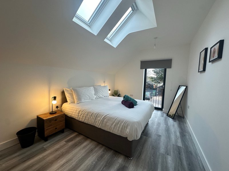 Bright modern bedroom with double bed, skylight windows, wooden nightstand and wall art