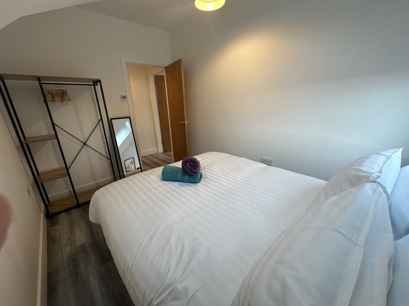 Bedroom with double bed, white bedding, wooden doors, and metal clothing rack