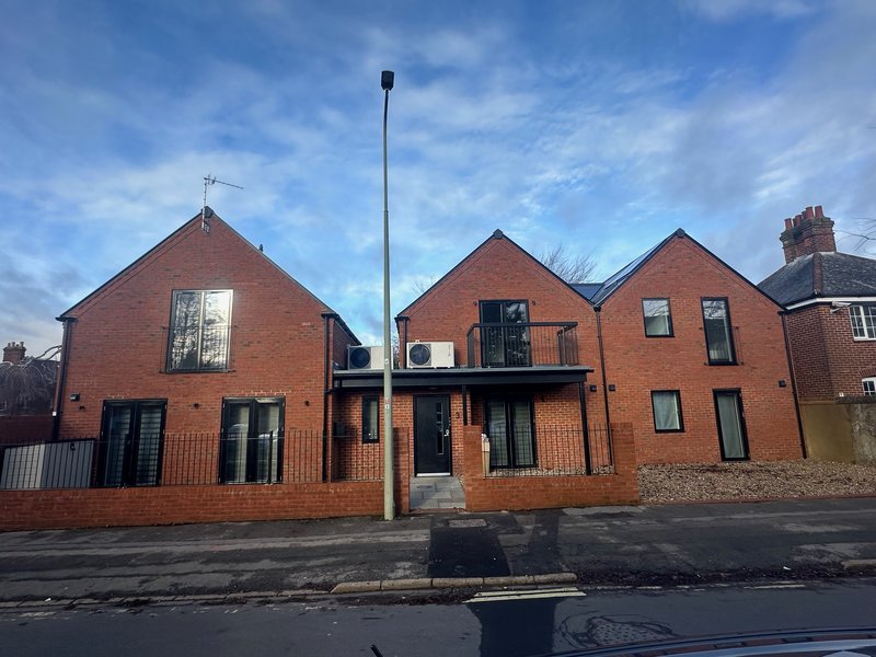 Modern red-brick residential building with pitched roofs, multiple windows and entrance, street view