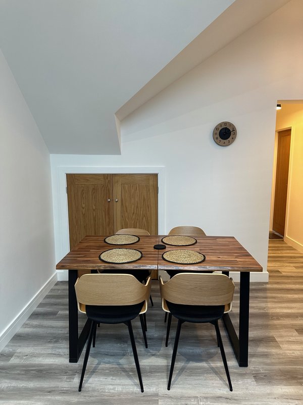 Dining area with wooden table, four beige chairs, place settings, and wooden cabinet
