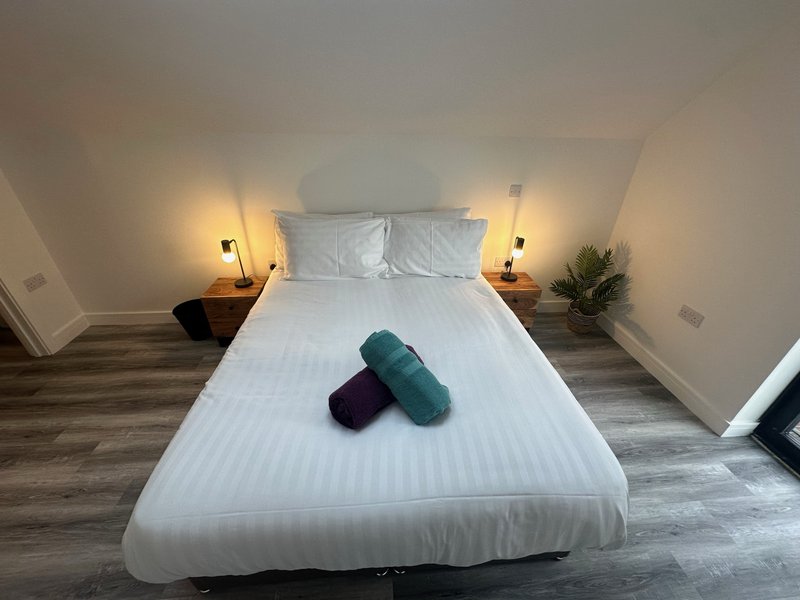 Modern bedroom with white bed, two rolled towels, bedside lamps and potted plant
