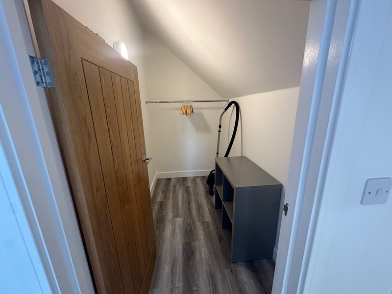 Narrow hallway with wooden door, black storage unit, clothes rail and vinyl flooring