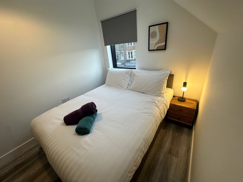 Small bedroom with double bed, wooden floor, bedside table and window with blind