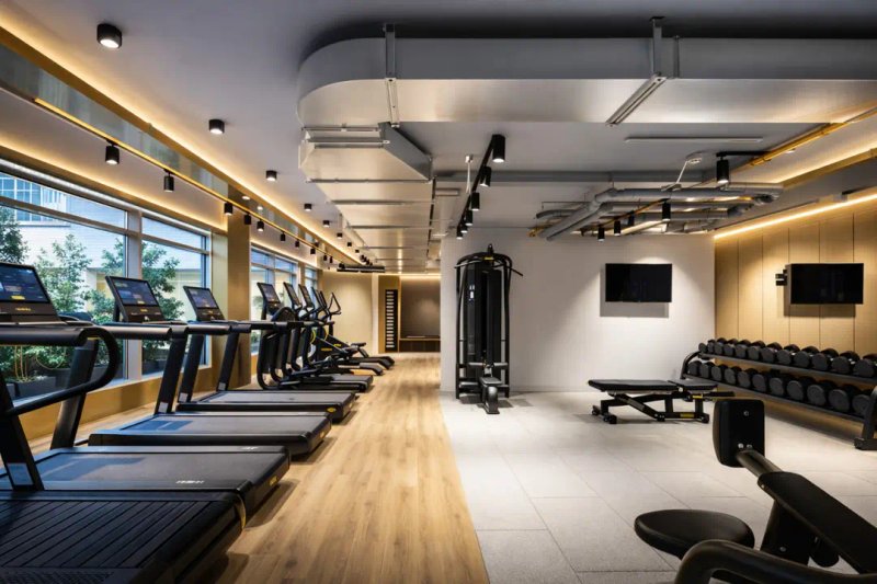 Modern gymnasium with treadmills, weight equipment, and dumbbells under bright ceiling lights
