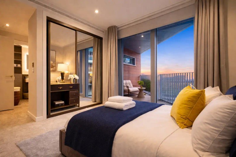 Modern bedroom with double bed, large mirror, yellow cushion, and balcony with sunset view