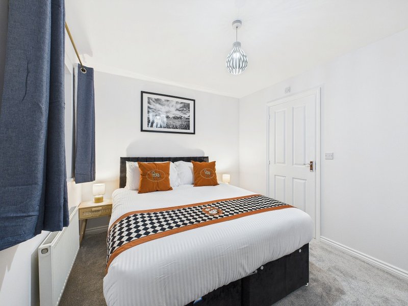 Bedroom with double bed, orange and white pillows, checkered throw blanket, pendant light fixture