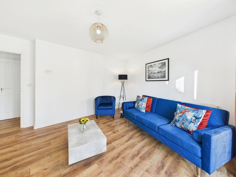 Bright living room with blue sofa, armchair, wooden flooring and white walls