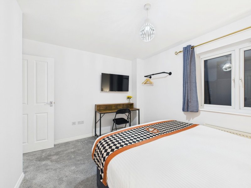 Bright bedroom with double bed, wall-mounted TV, desk, pendant light and window with blue curtains