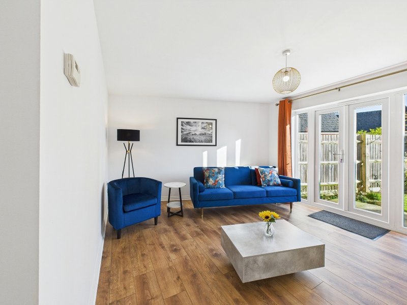 Bright living room with blue sofa and armchair, wooden floor, white walls and patio doors