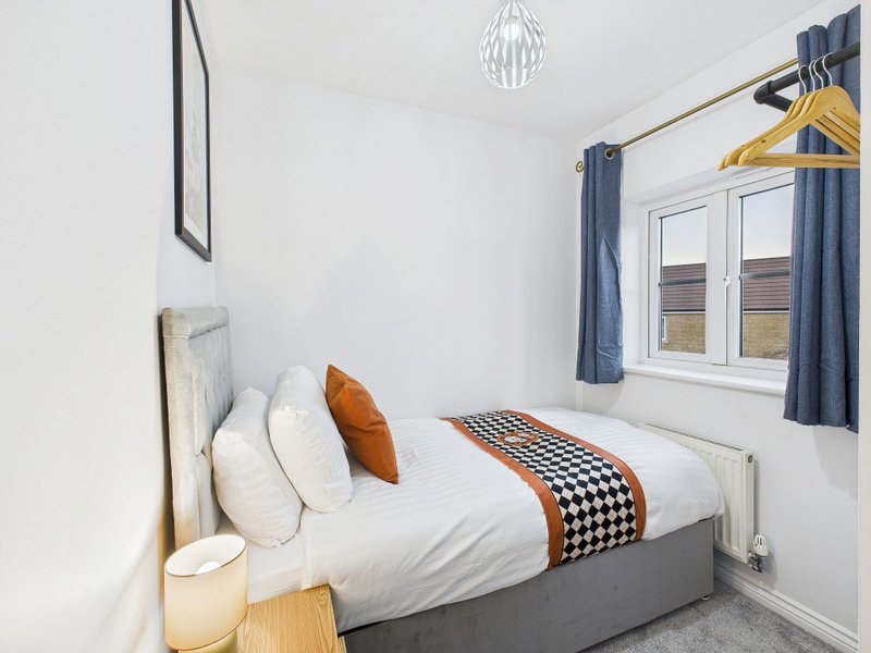 Small bedroom with single bed, white bedding, houndstooth throw and decorative pillows