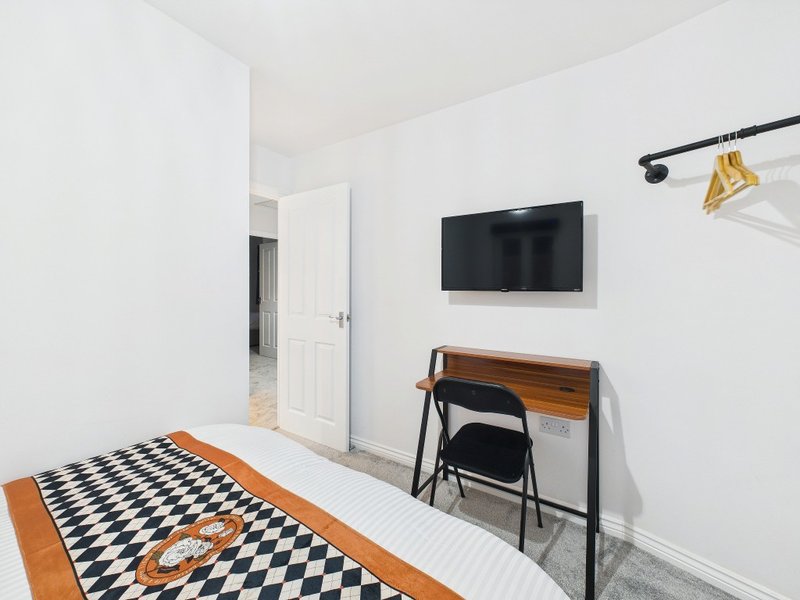 Modern bedroom with desk, chair, wall-mounted TV, and geometric patterned rug