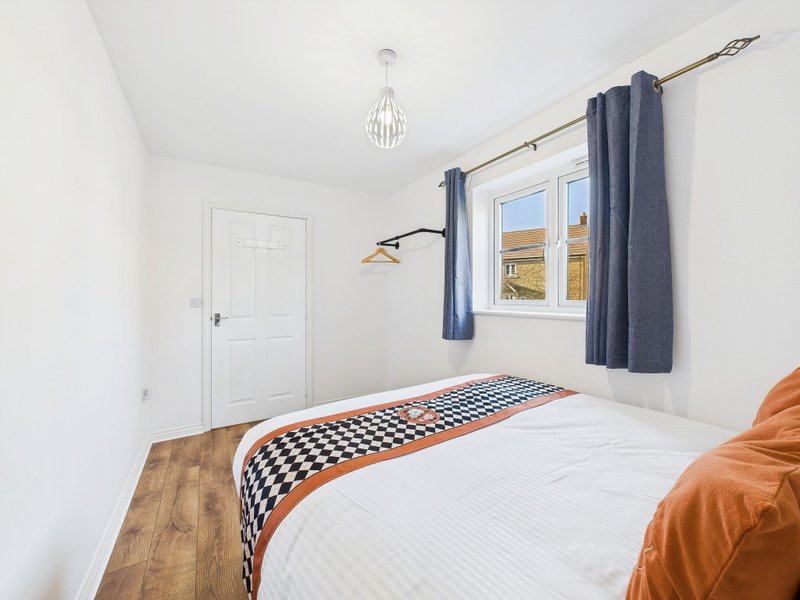 Bright bedroom with single bed, geometric bedding, window with blue curtains, pendant light