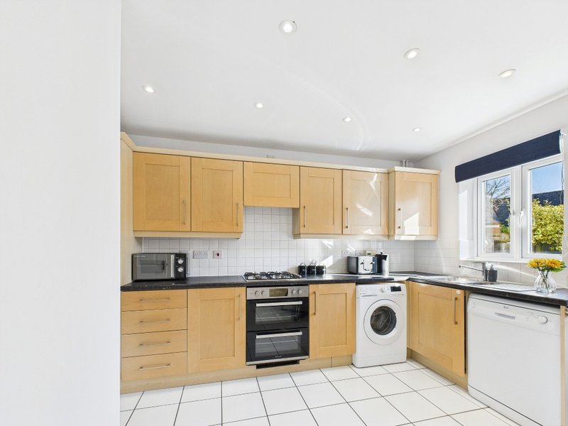 Modern kitchen with light wood cabinets, stainless steel appliances, and white tile flooring