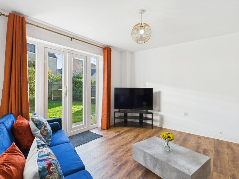 Bright living room with blue sofa, orange curtains, TV, wooden floor and garden view