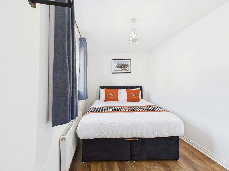 Modern bedroom with double bed, orange cushions, pendant light and wooden floor