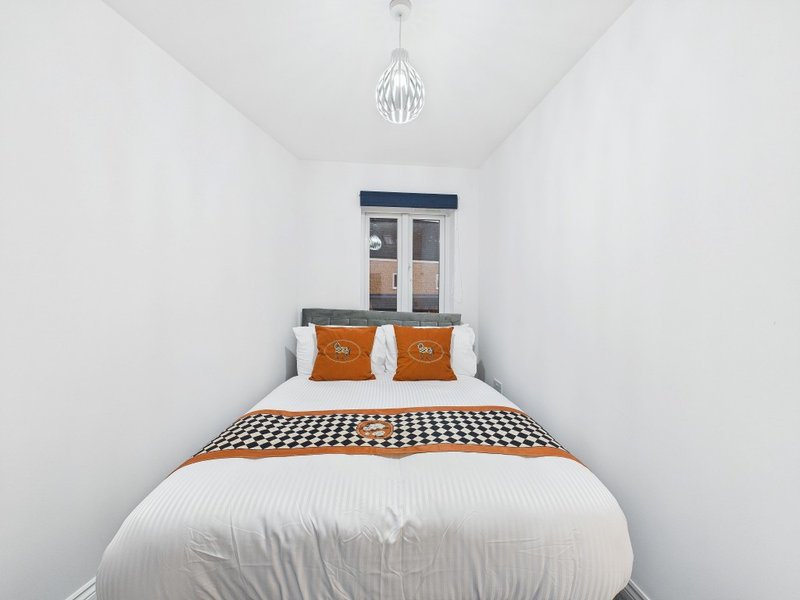 Small bedroom with double bed, orange cushions, checkered bedding, and pendant light fixture