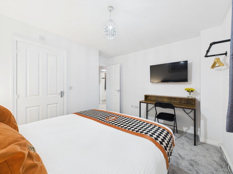 Modern bedroom with double bed, wall-mounted TV, desk, and pendant light fixture