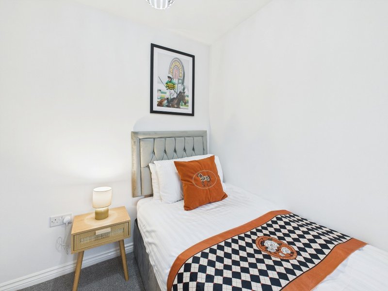 Bright bedroom with single bed, wooden nightstand, framed wall art and orange accent cushion