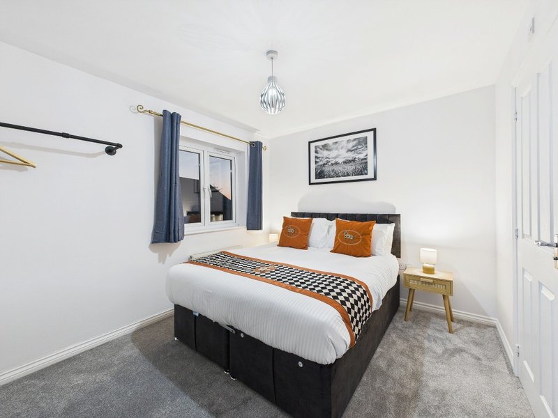 Modern bedroom with double bed, orange and white bedding, wooden nightstand, and window with blue curtains