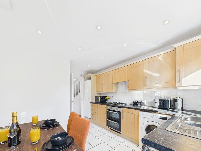 Modern kitchen with wooden cabinets, white walls, dining table set with place settings and champagne bottle