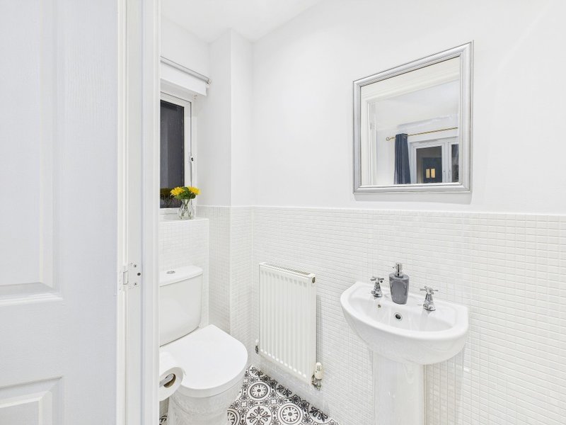 Clean white bathroom with pedestal sink, toilet, heated radiator and framed mirror