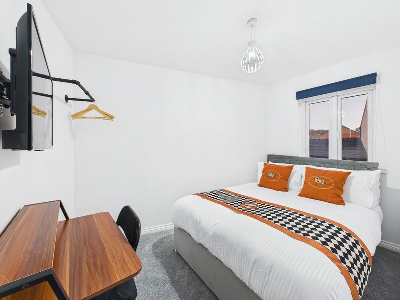 Modern bedroom with double bed, orange cushions, wooden desk, and pendant light fixture