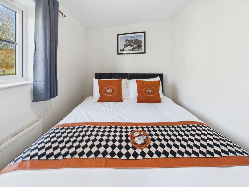 Bright bedroom with double bed, geometric patterned bedding, orange cushions and window with blue curtains