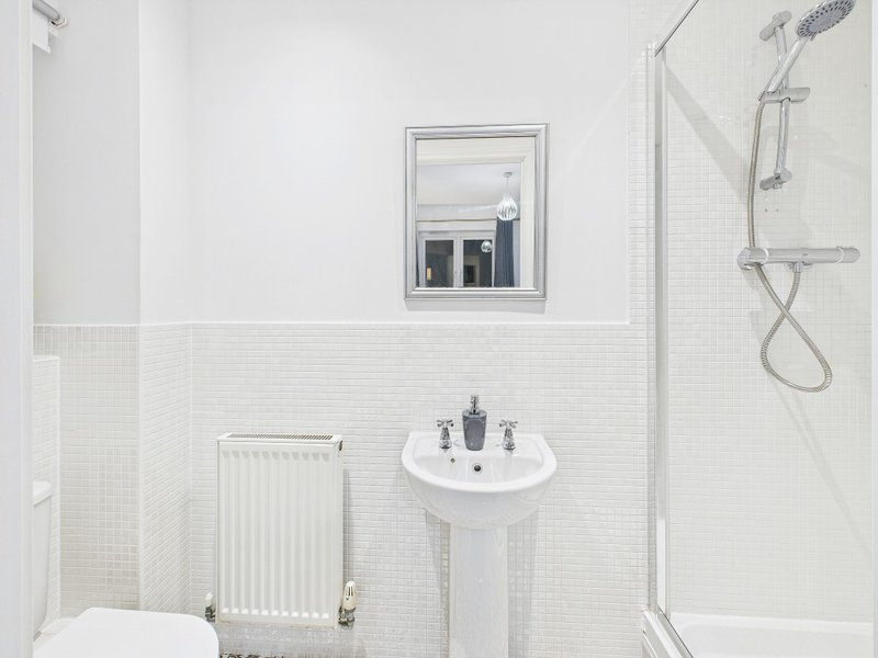 Clean white bathroom with pedestal sink, toilet, radiator and shower enclosure