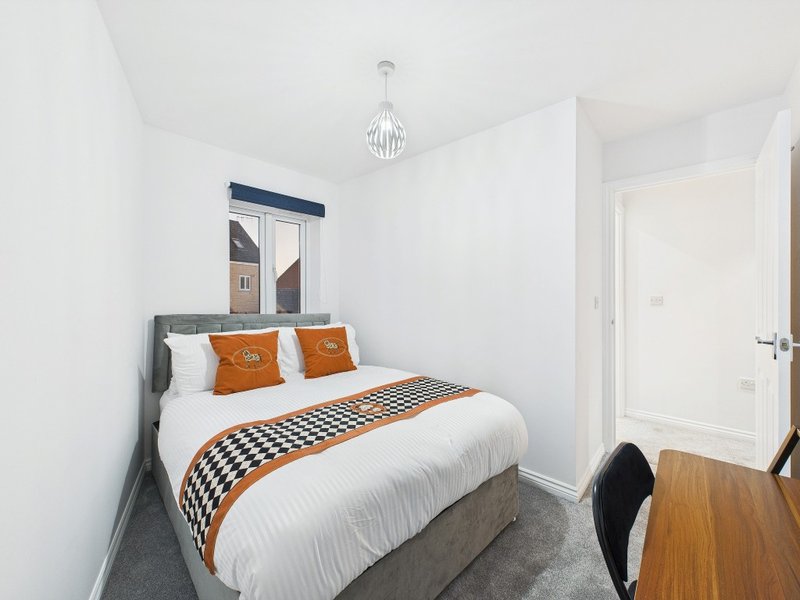 Modern bedroom with double bed, orange and white bedding, pendant light and white walls