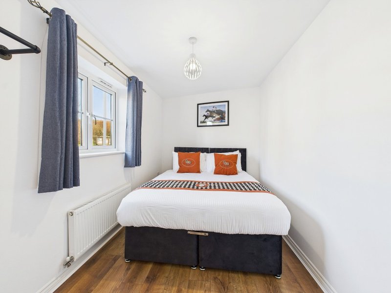 Small bedroom with double bed, blue curtains, wooden floor and pendant light