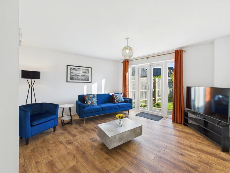 Bright living room with blue sofa and armchair, wooden floor, white walls and patio doors