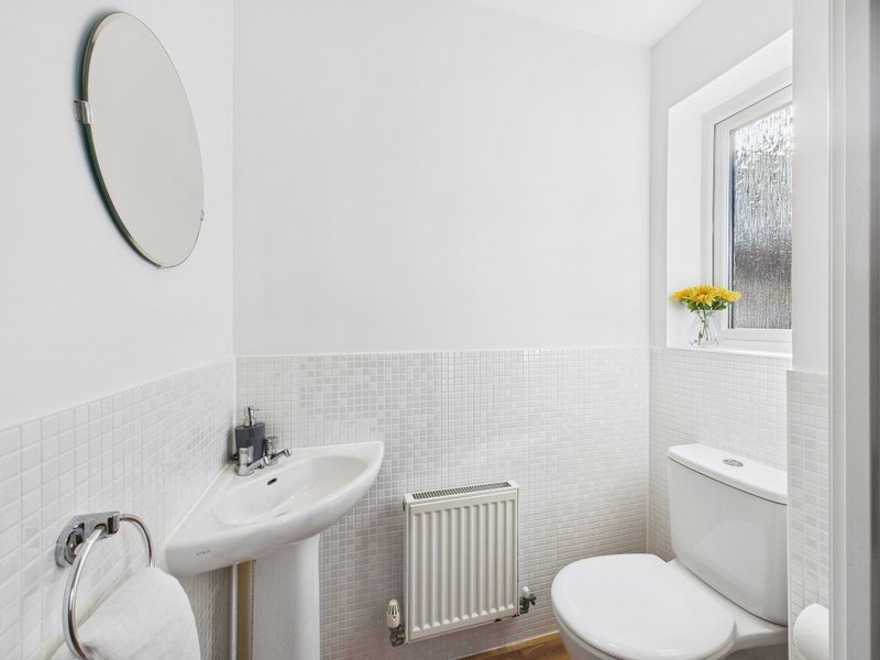 Clean white bathroom with pedestal sink, toilet, radiator and round mirror
