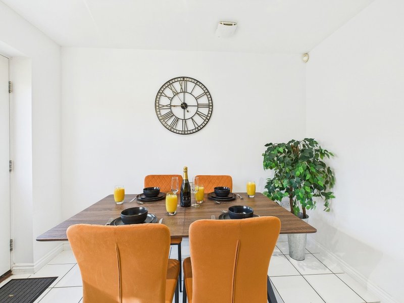 Dining room with wooden table, orange chairs, wall clock and potted plant